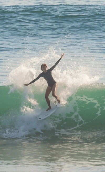 Woman in a wetsuit balancing with her arms out on a small wave, foam trailing behind her